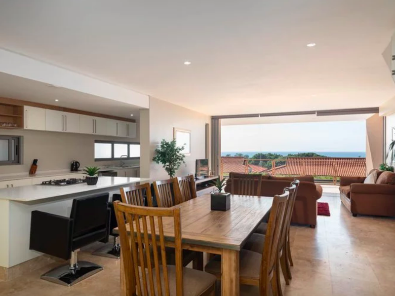 Spacious open-plan living and dining area featuring a modern kitchen with stone countertops, gas hob, and seamless flow to a balcony with ocean views.
