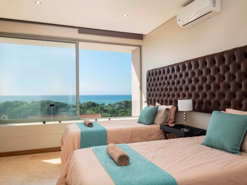 A well-appointed bedroom featuring stone flooring, recessed lighting, an air conditioning unit, and a large sliding glass door offering expansive ocean views.