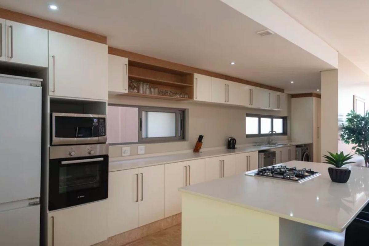 Modern kitchen featuring sleek white cabinetry, stone countertops, a central island with a gas cooktop, and integrated appliances.