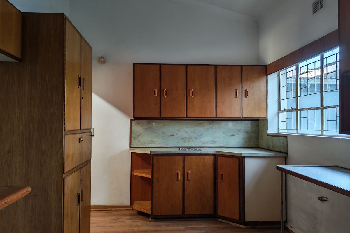 A dated kitchen featuring original wooden cabinetry, laminate countertops, and a leaded glass window, offering a blank canvas for a modern renovation.