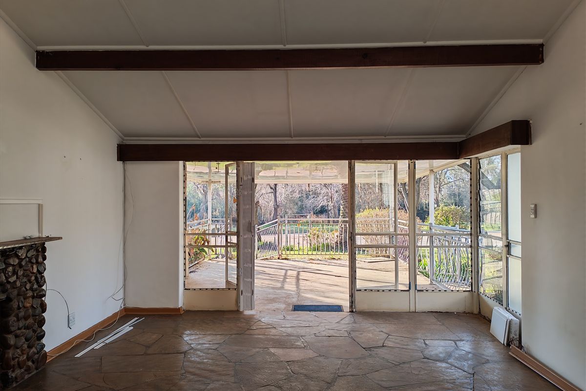 Spacious living area featuring a rustic stone fireplace, flagstone flooring, and exposed timber beams, opening directly onto a covered outdoor patio.