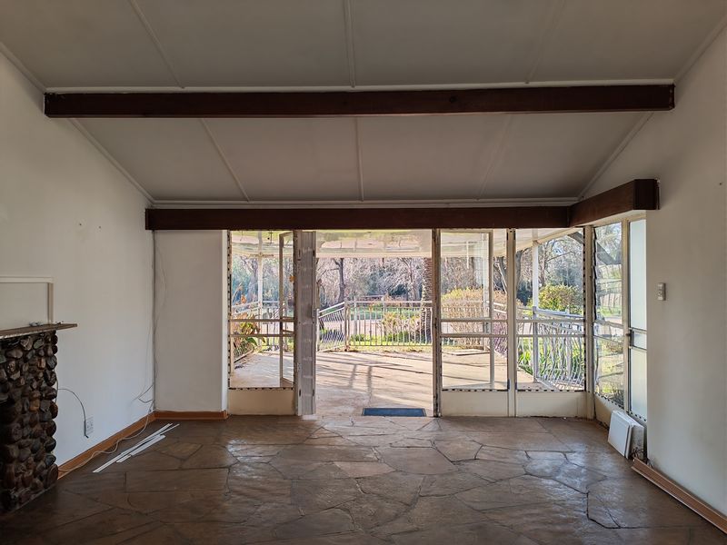 Spacious living area featuring a rustic stone fireplace, flagstone flooring, and exposed timber beams, opening directly onto a covered outdoor patio.