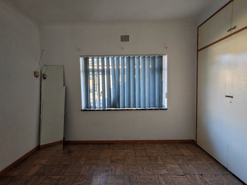 A vacant bedroom featuring original parquet flooring, built-in cupboards, and vertical window blinds, offering a blank canvas for renovation.