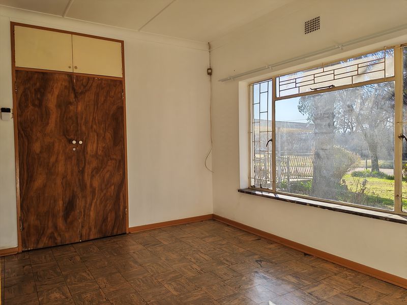 An empty bedroom featuring original parquet flooring, a built-in wooden wardrobe, and large steel-framed windows overlooking the garden.