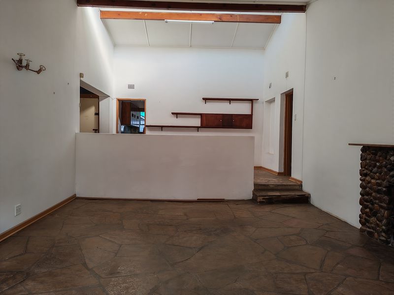 Spacious living area featuring rustic flagstone flooring, a stone fireplace, exposed timber beams, and a skylight, offering a blank canvas for renovation.