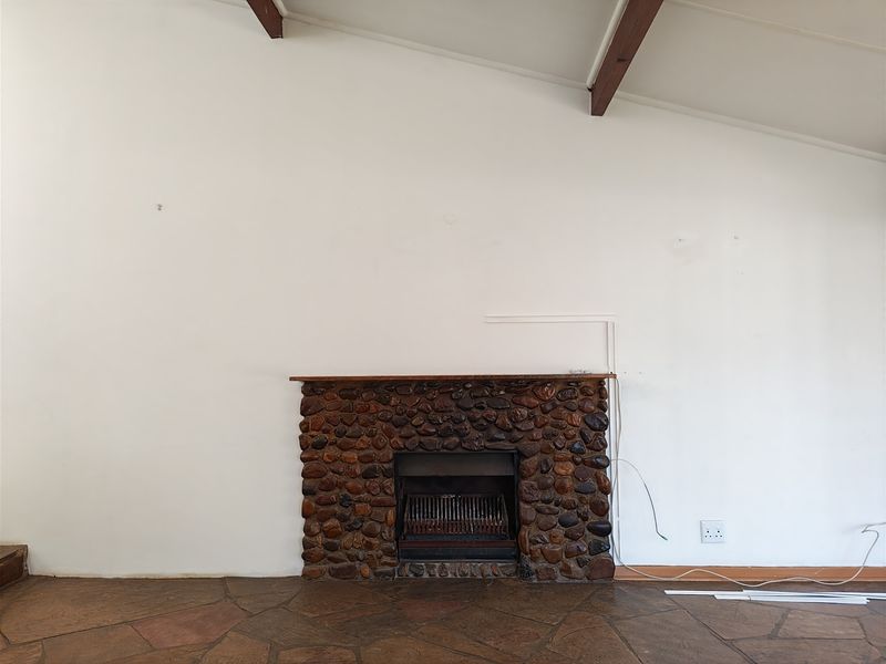 Spacious living area featuring a rustic stone fireplace, exposed timber ceiling beams, and traditional flagstone flooring in a neutral, open setting.