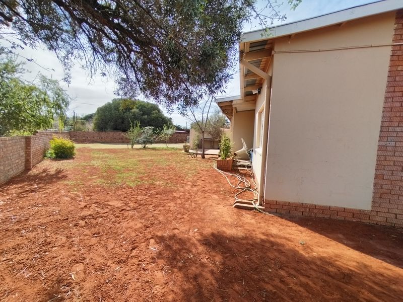 Rear exterior view of the property featuring a large garden area with brick boundary walls and exposed soil ground cover.