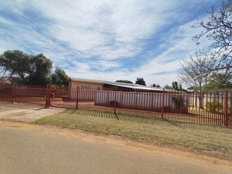 Front view of the property featuring a secure metal perimeter fence, gated entrance, and a single-story dwelling with a metal roof.