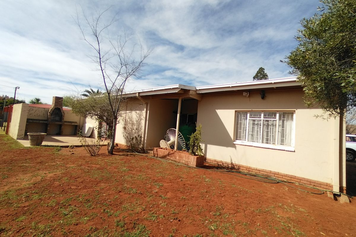 Rear view of the property featuring a built-in brick braai area, paved patio space, and security bars on the windows.