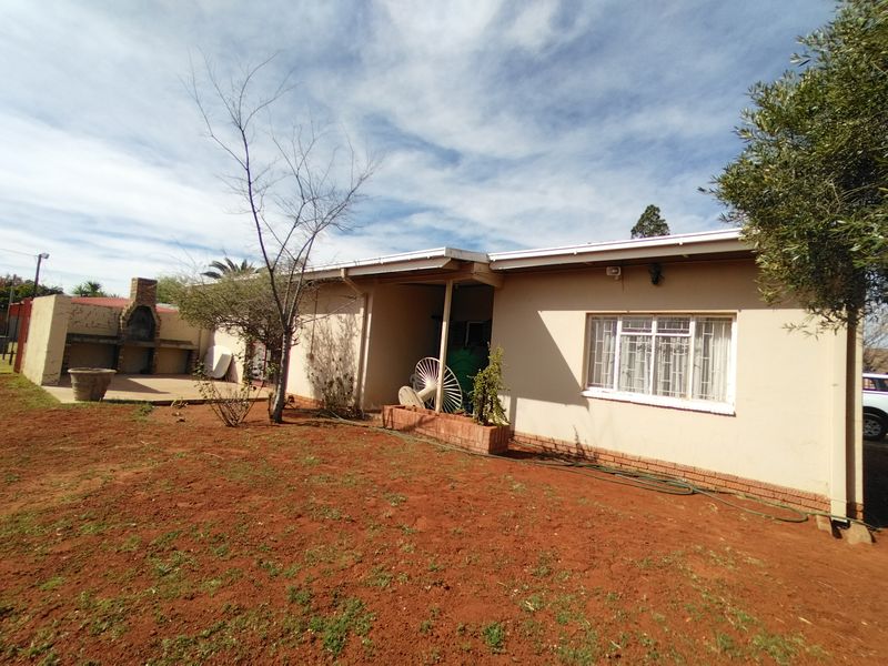 Rear view of the property featuring a built-in brick braai area, paved patio space, and security bars on the windows.