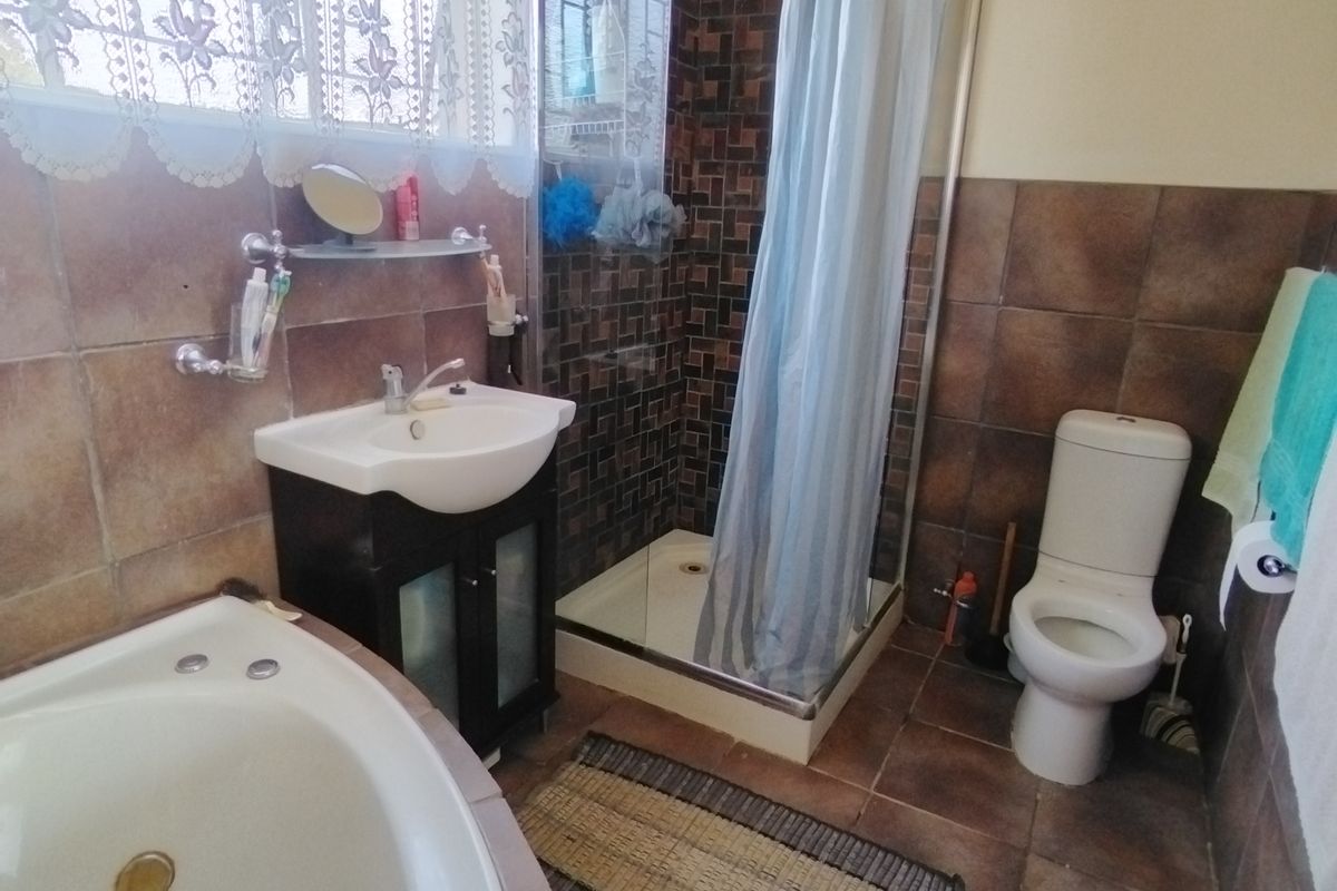A functional bathroom featuring a corner bathtub, separate shower enclosure, vanity basin, and toilet with brown tiled finishes.