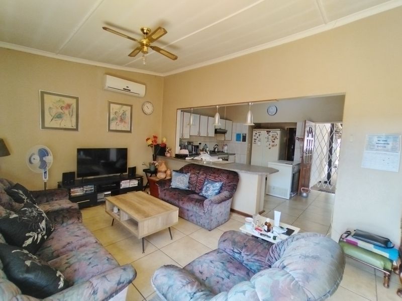 Open plan living area featuring tiled floors, a breakfast bar connecting to the kitchen, and a ceiling fan with wall-mounted air conditioning.