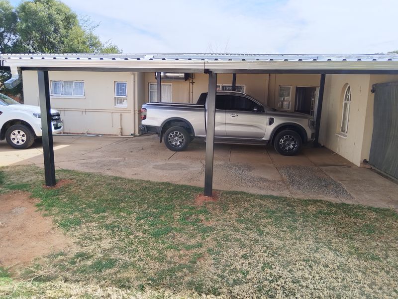 A functional outdoor carport area with a metal roof structure and concrete driveway, providing covered parking space for vehicles.
