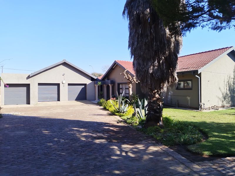 Front view of the property featuring a triple garage, paved driveway, and well-maintained garden area.