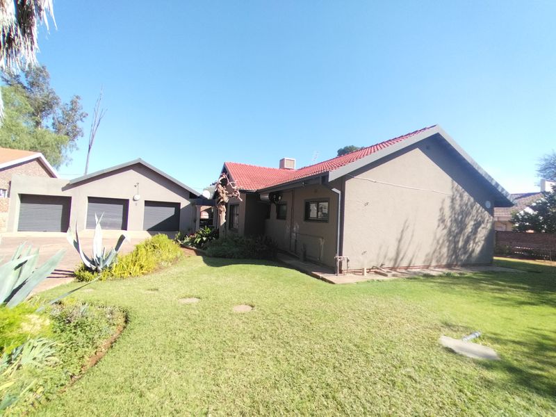 A view of the rear exterior of the house featuring a well-maintained lawn, landscaped garden, and a detached double garage with roller doors.