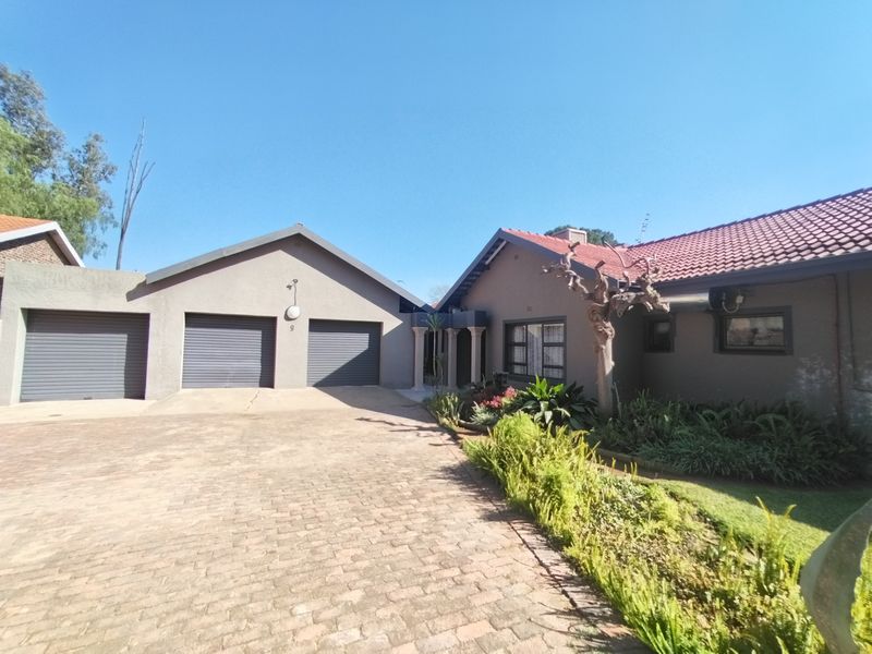 Front view of the property featuring a triple garage with roller shutter doors, a paved driveway, and a well-established garden.