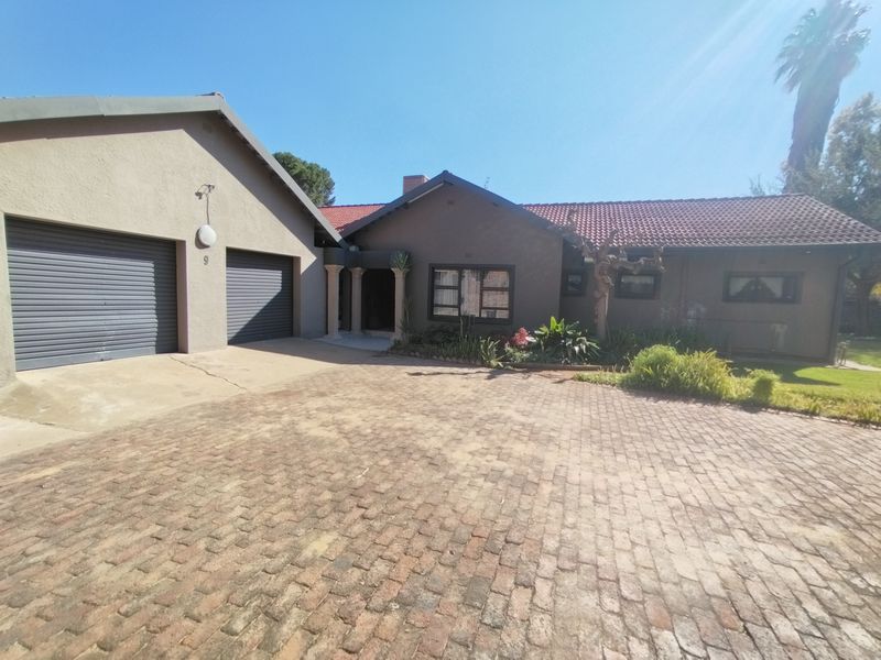 Front elevation of a residential property featuring a double garage, brick paved driveway, and a covered entrance with decorative columns.