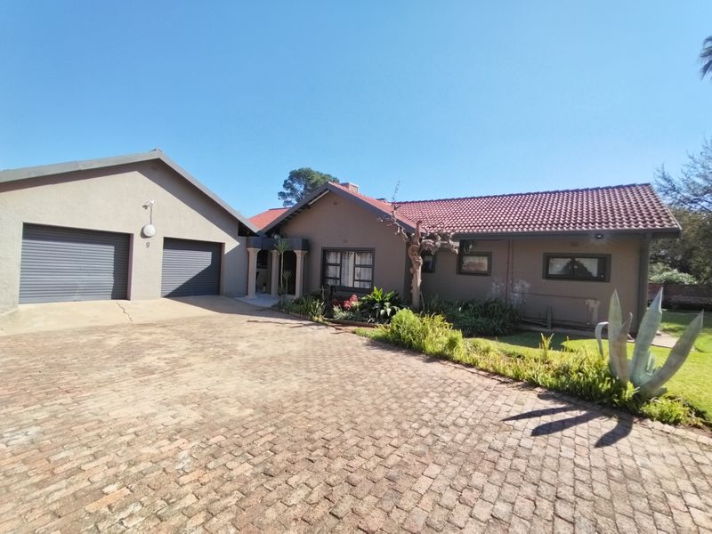 Front view of a single-story house featuring a paved driveway, double garage, and tiled roof with established garden beds.