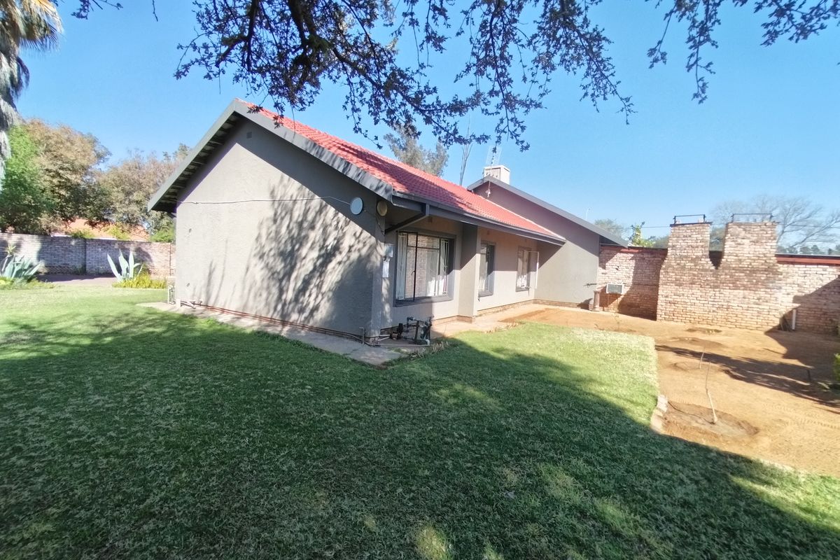 Rear view of the house featuring a tiled roof, brick chimney, and a spacious garden with lawn and boundary wall.