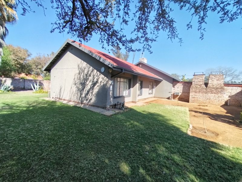 Rear view of the house featuring a tiled roof, brick chimney, and a spacious garden with lawn and boundary wall.