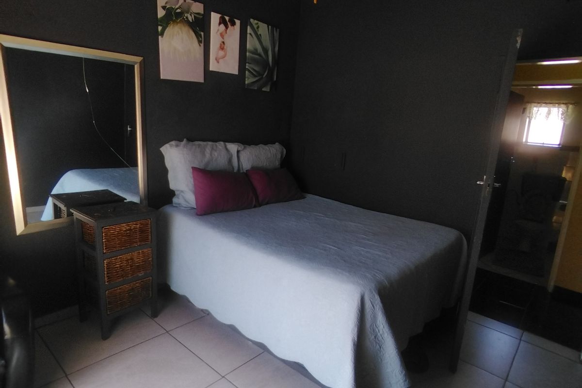 A bedroom featuring dark painted walls, tiled flooring, and a ceiling fan, with an adjacent view into a bathroom area.