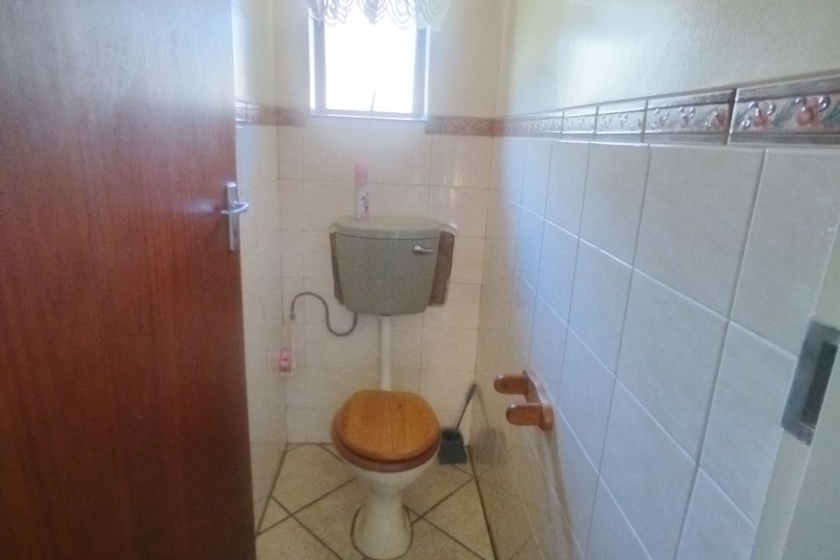A compact guest bathroom featuring dated sanitaryware, ceramic wall and floor tiling, and a small window for natural light.