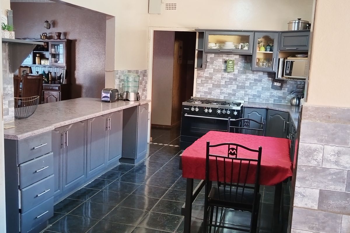 A functional kitchen featuring grey cabinetry, a gas stove, tiled backsplash, and a breakfast counter, with direct access to the adjacent dining area.