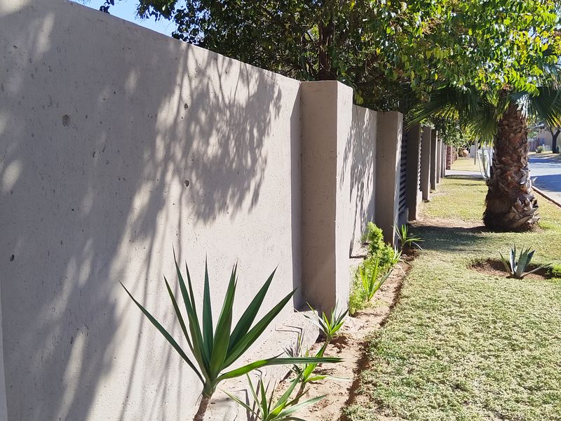 A view of the property's concrete boundary wall and landscaped verge, featuring established trees and garden plantings along the street frontage.