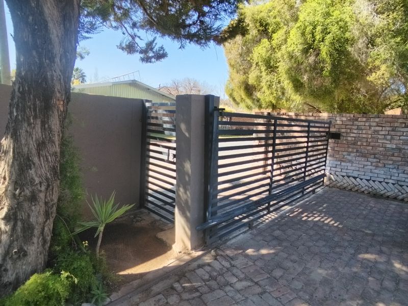 A secure front entrance featuring a modern horizontal slat sliding gate, brick paved driveway, and solid boundary walling.