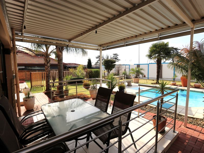 Covered outdoor patio area featuring a stainless steel balustrade, overlooking a private swimming pool and landscaped garden.