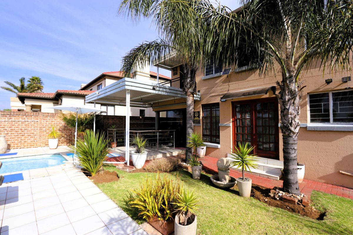 Rear exterior view featuring a swimming pool, a covered patio area, landscaped garden, and direct access to the home via french doors.