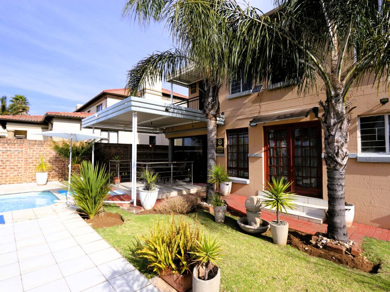 Rear exterior view featuring a swimming pool, a covered patio area, landscaped garden, and direct access to the home via french doors.