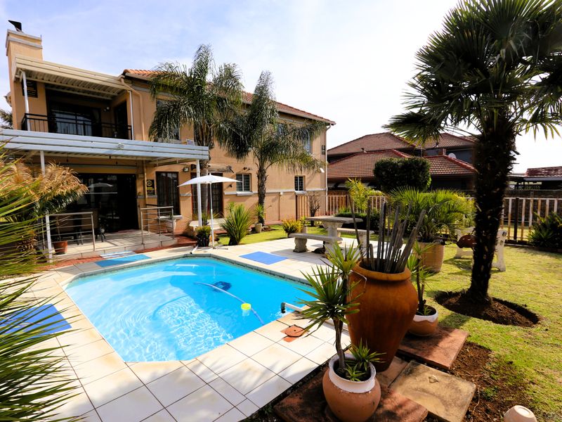 Rear exterior view featuring a swimming pool with tiled surround, a covered patio area, and a well-maintained garden with established trees.