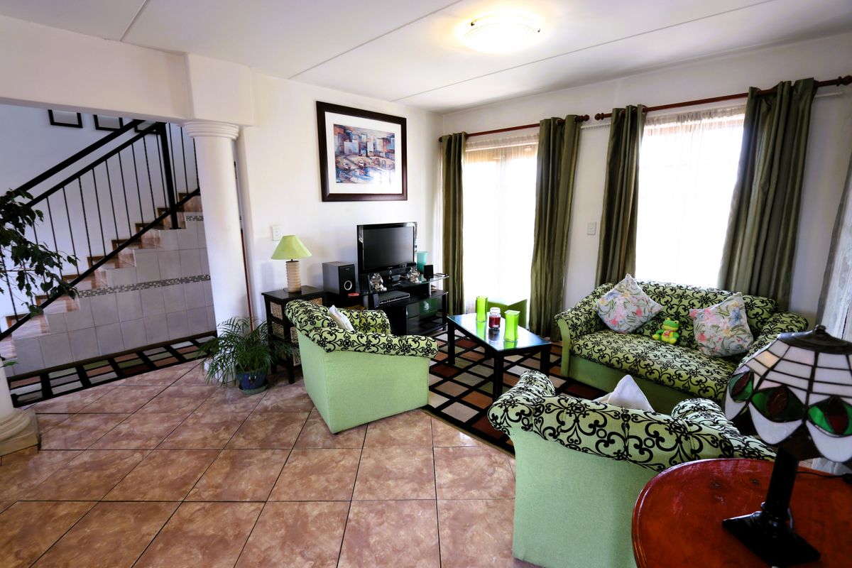 A spacious living room featuring tiled flooring, a decorative column, and an adjacent staircase with a metal railing.