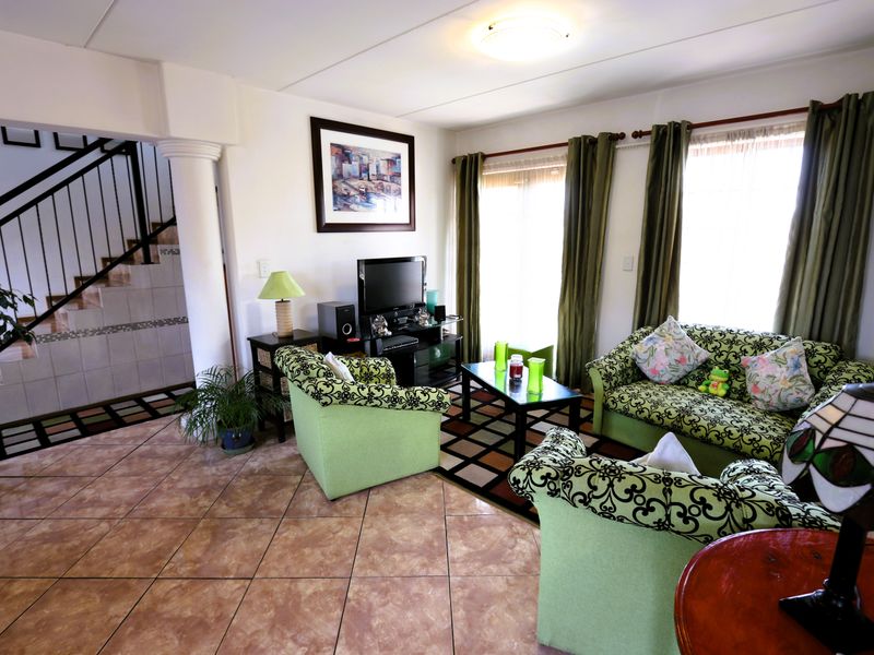 A spacious living room featuring tiled flooring, a decorative column, and an adjacent staircase with a metal railing.