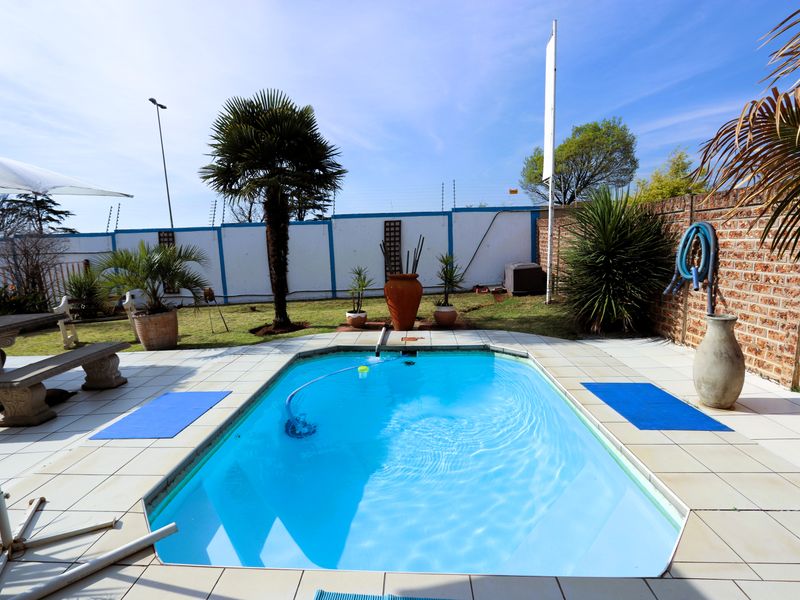 Outdoor pool area featuring a swimming pool with tiled surround, set within a private garden enclosed by brick boundary walls and electric fencing.