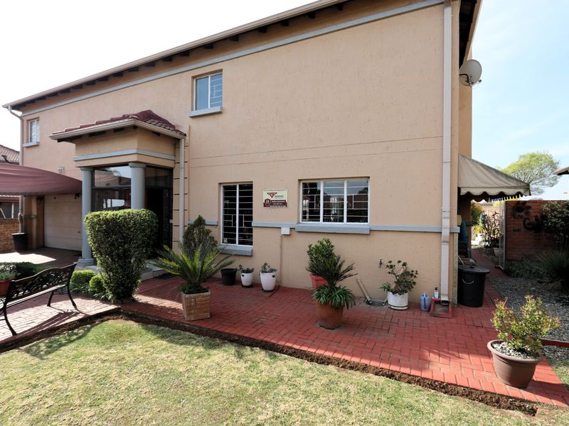 Rear view of the house featuring a brick paved patio area, security bars on windows, and an attached awning.