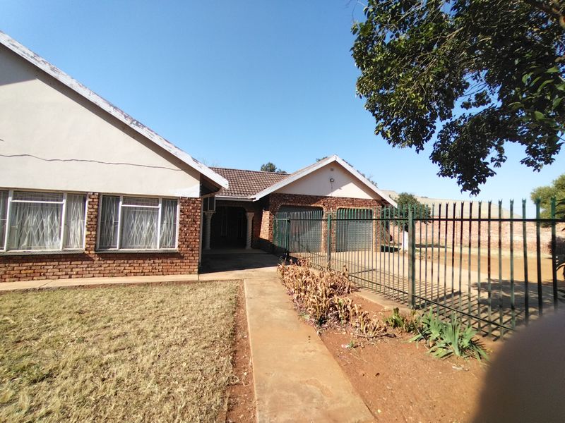 Front view of a single-story brick house featuring a double garage, security fencing, and a paved walkway leading to the entrance.