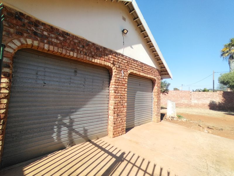 A double garage featuring exposed brick detailing and metal roller doors, situated on a concrete driveway with an adjacent open yard area.