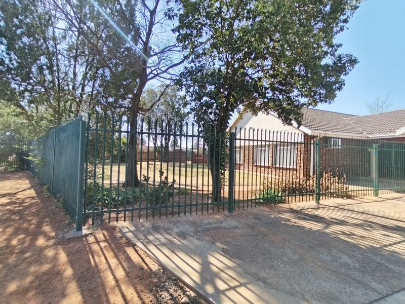 Front view of the property featuring a brick facade, tiled roof, and secure steel palisade fencing enclosing the front garden and concrete driveway.