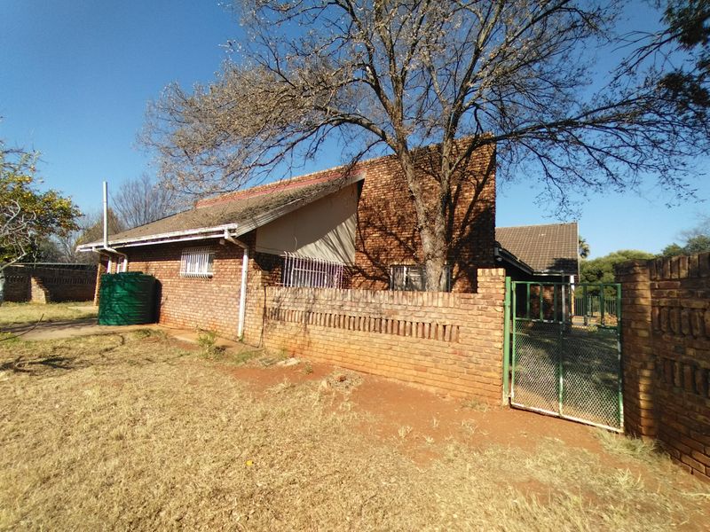 Rear view of a face brick house featuring a tiled roof, security gates, and an external water storage tank set within a large garden area.