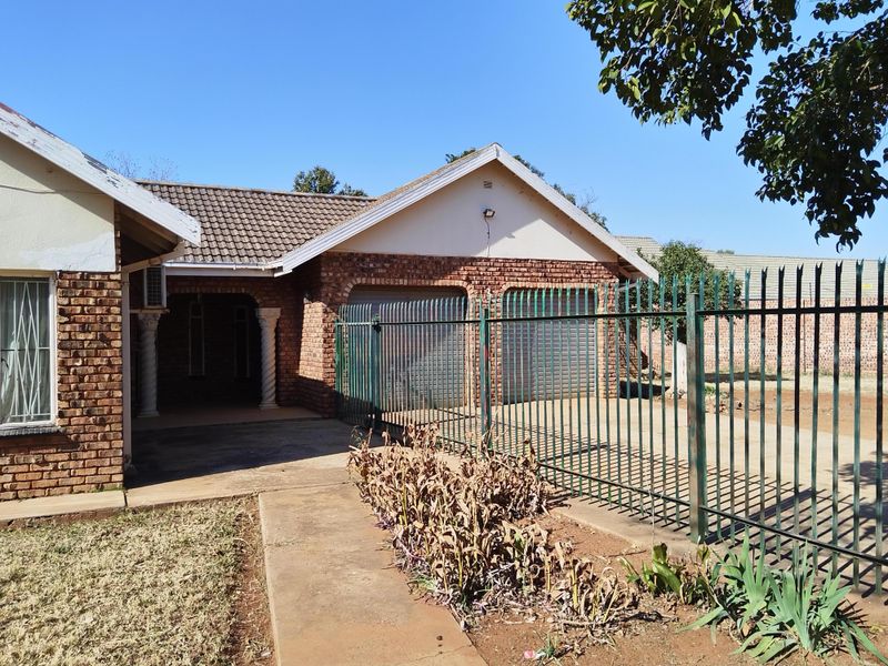 Front view of a face brick house featuring a double garage, concrete driveway, and secure steel perimeter fencing.