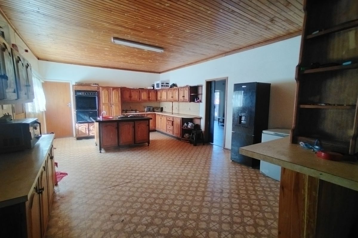 Spacious kitchen featuring extensive wooden cabinetry, a central island, built-in oven, and hob, offering a functional layout with significant potential for modern renovation.