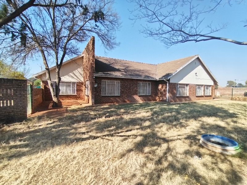 Front view of a single-story face-brick house featuring a tiled roof, security bars on windows, and a large, dry garden area.