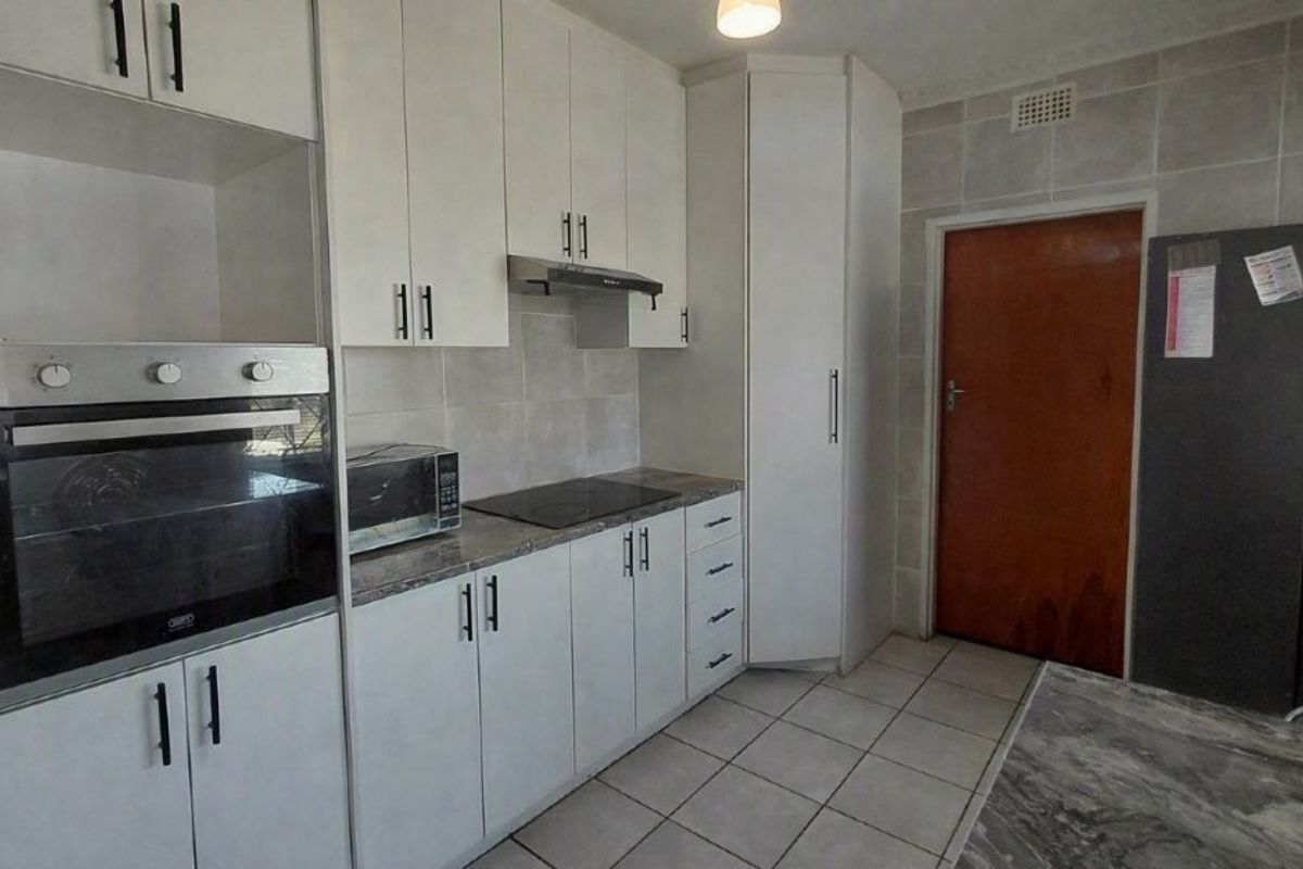 A functional kitchen featuring white cabinetry, built-in oven, electric hob, extractor fan, and tiled flooring with a neutral backsplash.