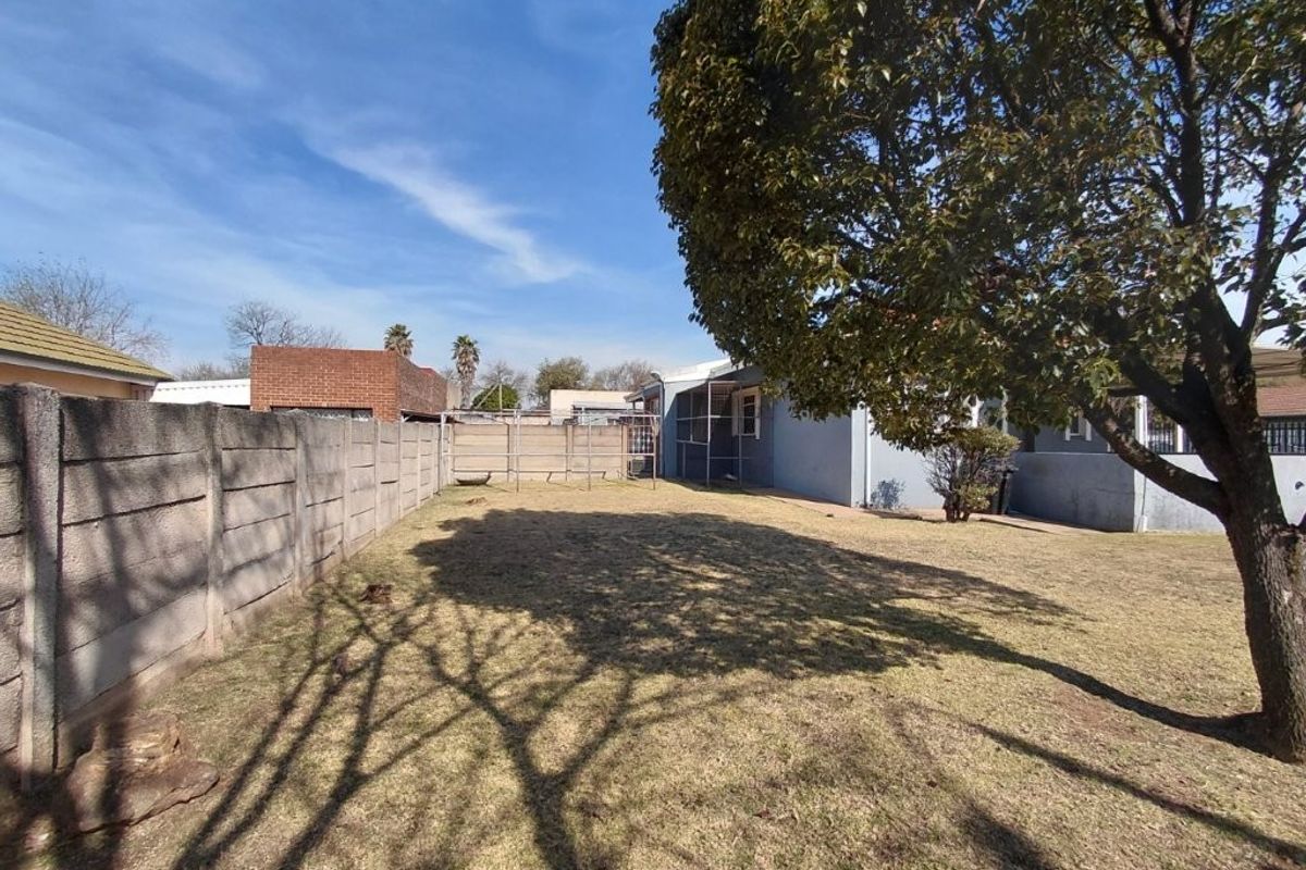 A spacious rear garden featuring a large mature tree, a precast concrete boundary wall, and a metal washing line area.