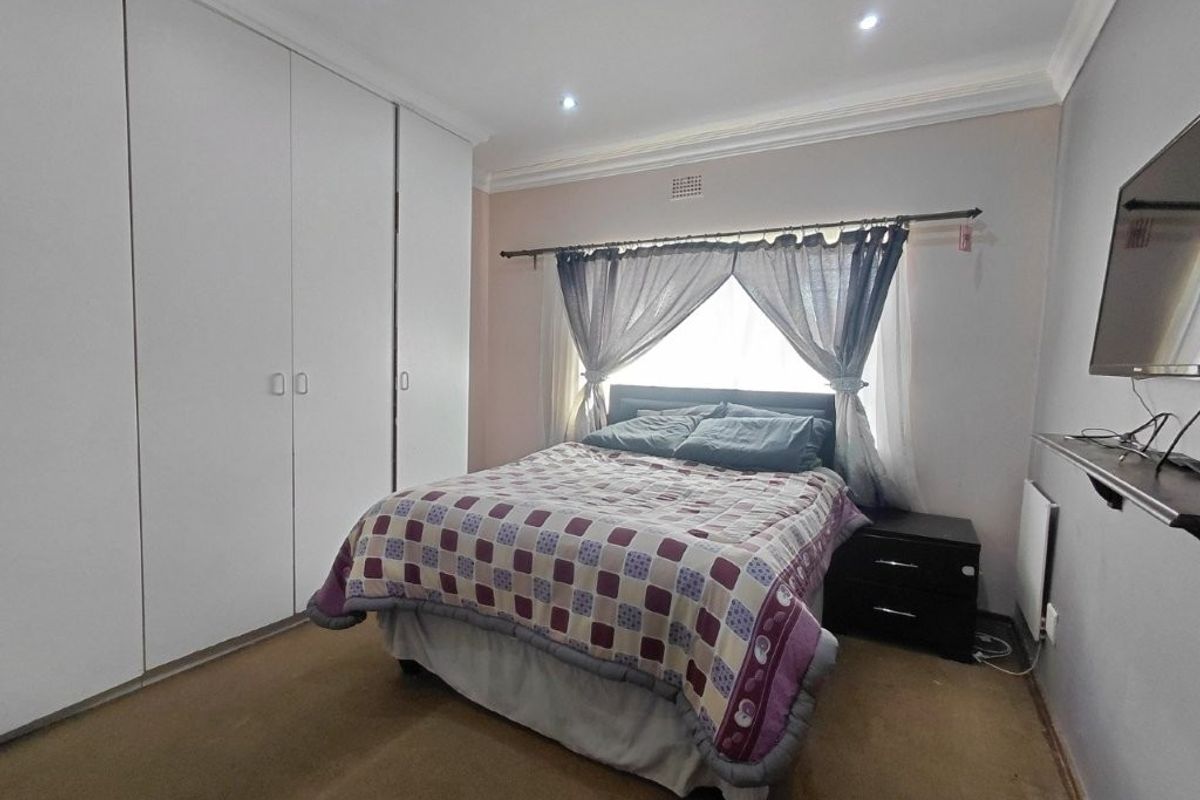 A functional bedroom featuring built-in cupboards, recessed downlighting, and a wall-mounted heater, providing a comfortable and practical living space.