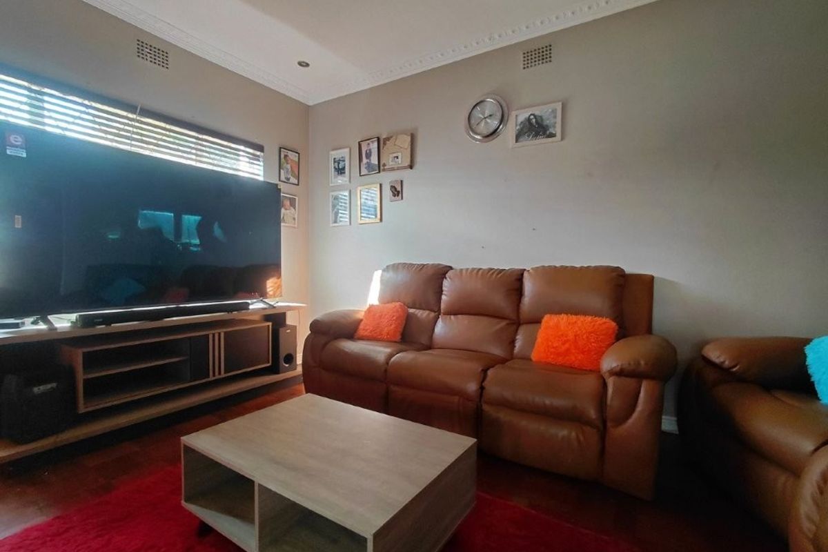 A comfortable living room featuring laminate flooring, recessed downlights, and decorative ceiling cornicing, providing a functional space for relaxation.
