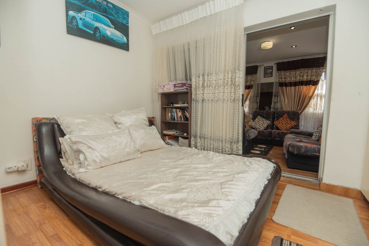 A bedroom featuring laminate flooring and a sliding door leading to an adjacent living area with recessed ceiling lighting.