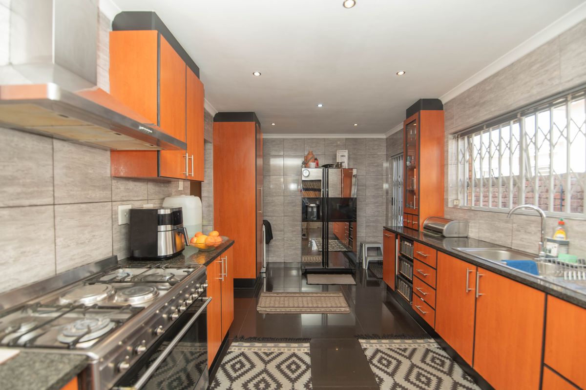 A functional kitchen featuring warm-toned wooden cabinetry, granite countertops, a gas stove with extractor fan, and modern tiled finishes throughout.